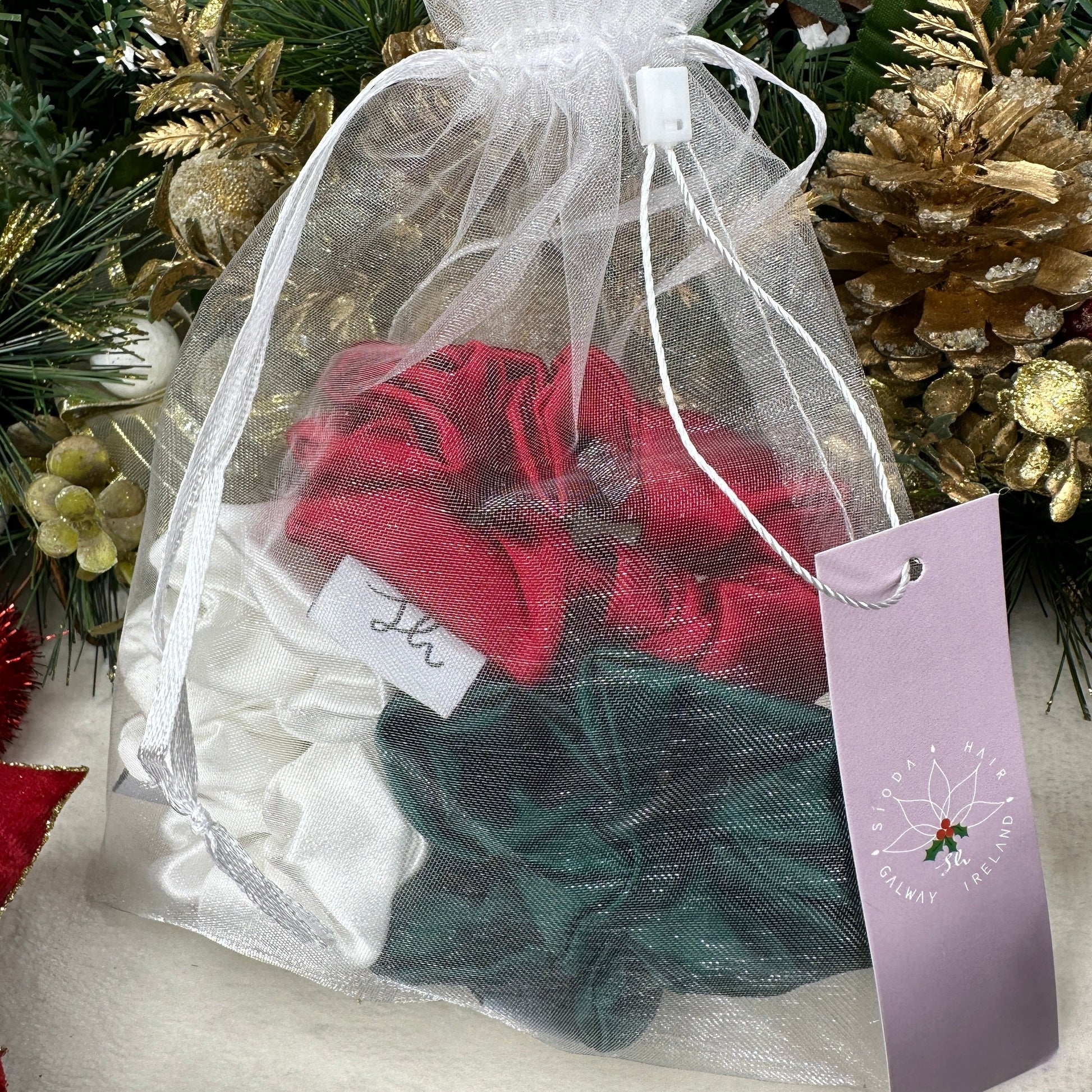 Sioda Hair Silky Range, The Christmas Collection 100% Mulberry Silk scrunchies in white, green and red set against a white powder effect surrounded by a christmas wreath, size medium, packaged in a white net pouch